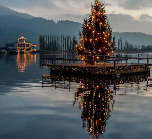 Ein großer geschmückter Weihnachtsbaum, der auf einer Hölzernen Plattform mitten im See steht